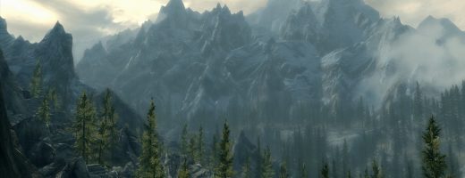 A screenshot from Elder Scrolls V: Skyrim. It's of mountains covered in pine forests, with wispy clouds in the sky.