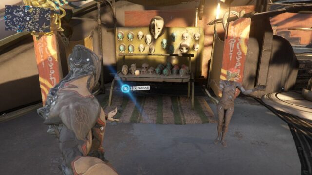 Screenshot from Warframe showing the vendor Nakak. She is a child wearing a paper-mache mask, her arms raised mid-gesture